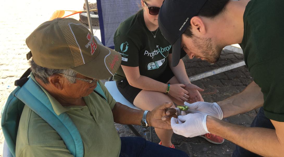 An intern screens a local for high blood sugar during a Health Fair in Belize Public Health intern tests the blood sugar levels of a patient in Belize